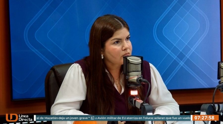 Mujer viendo hacia un lado con un micrófono frente a ella y una pantalla en el fondo