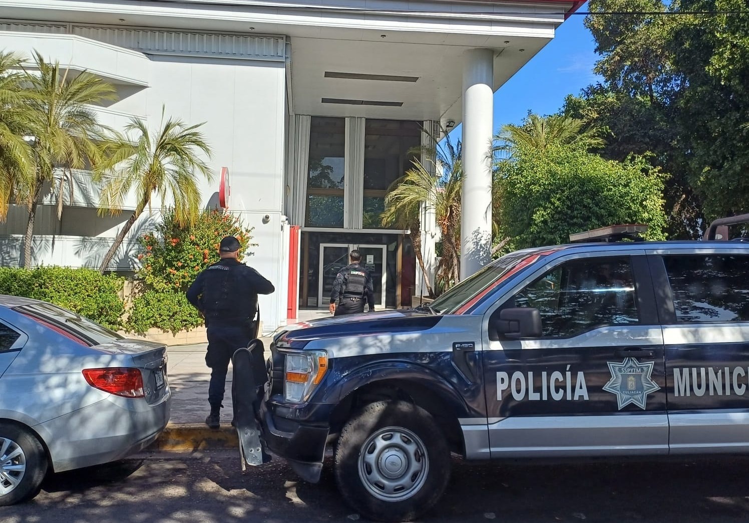 Dos policías municipales de pie y una patrulla estacionada frente a un banco en Culiacán