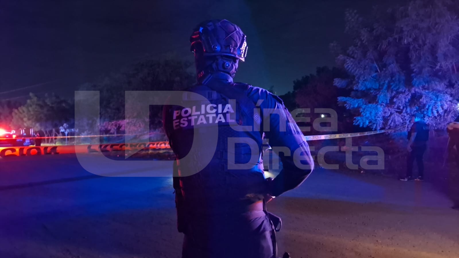 Elemento policiaco de espaldas y al fondo se observan unidades de emergencia y una cinta amarilla de precaución
