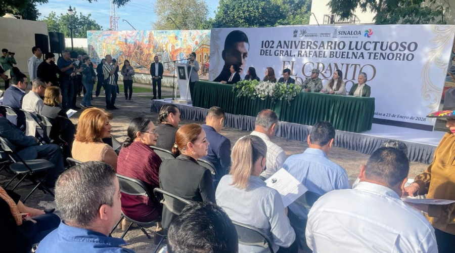 Personas en un escenario realizando un acto honorifico y personas sentadas en el publico