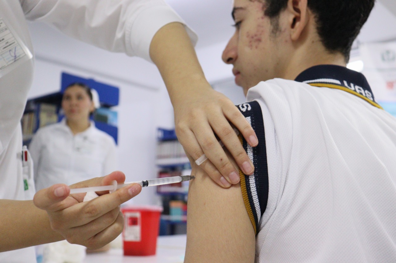 Medico aplicando vacuna a adolescente en el brazo izquierdo