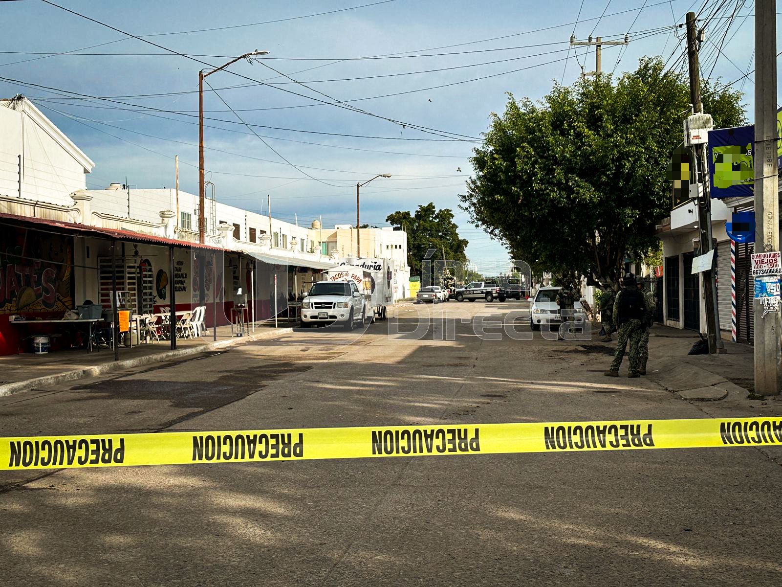 Cinta amarilla de precaución en una calle y al fondo policías y unidades cerrando el paso