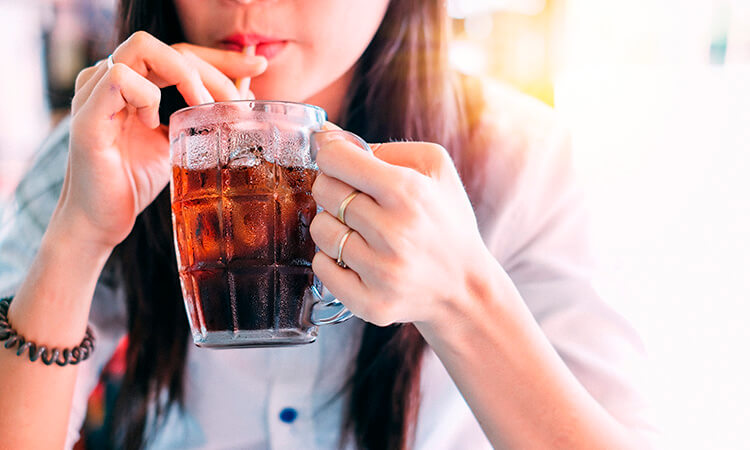Mujer tomando refresco en un vaso con popote sujetandolo con las manos