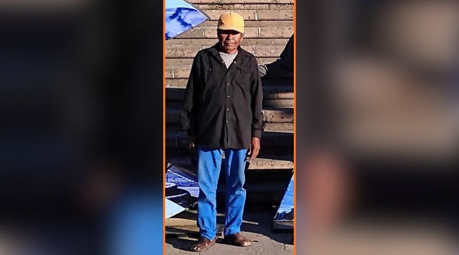 PErsona de pie con chamarra negra, pantalón de mezclilla y huaraches y gorra
