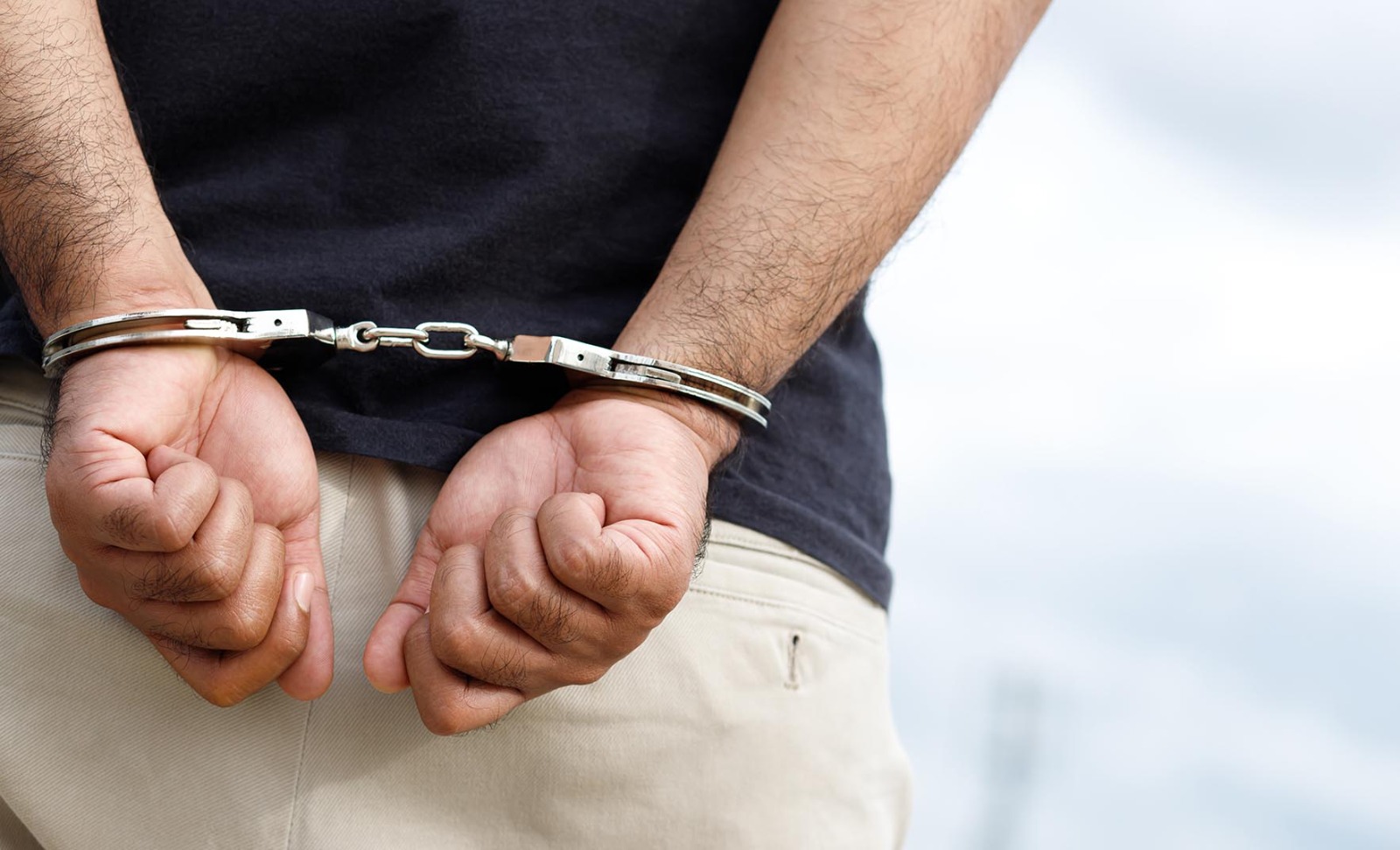 hombre esposado con las manos hacia atras con camiseta negra y pantalon
