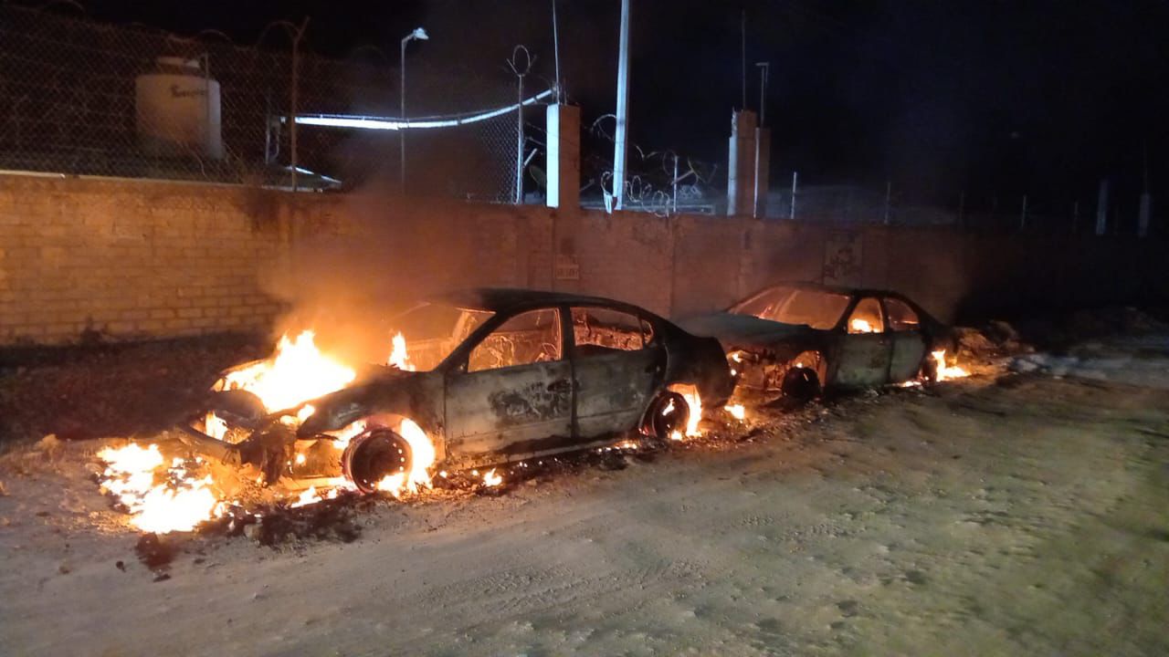 Vehículos calcinados y por las llamas en una calle a lado de una barda