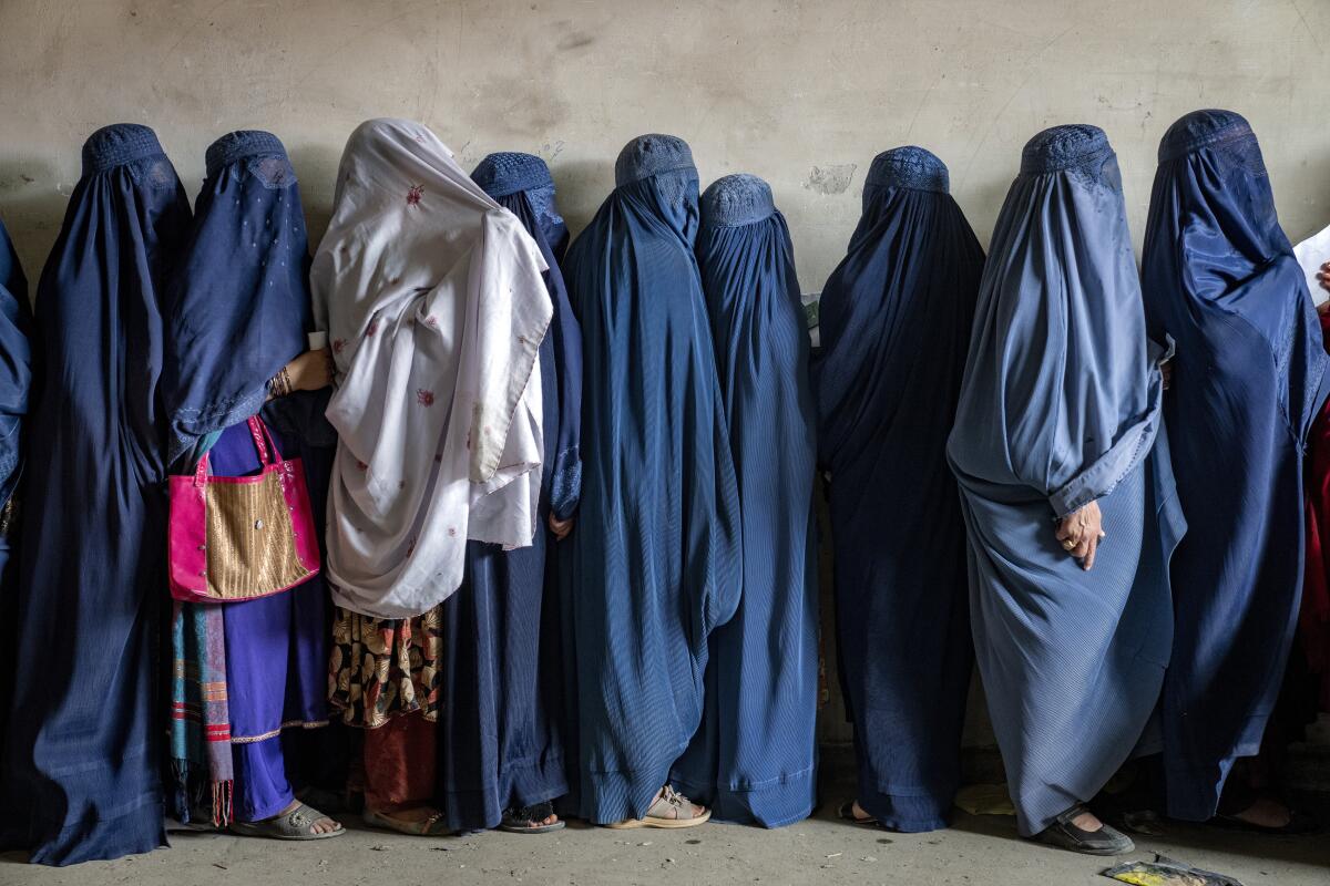 Mujeres afganas con vestidos que las cubren totalmente en una fila donde reparten alimentos