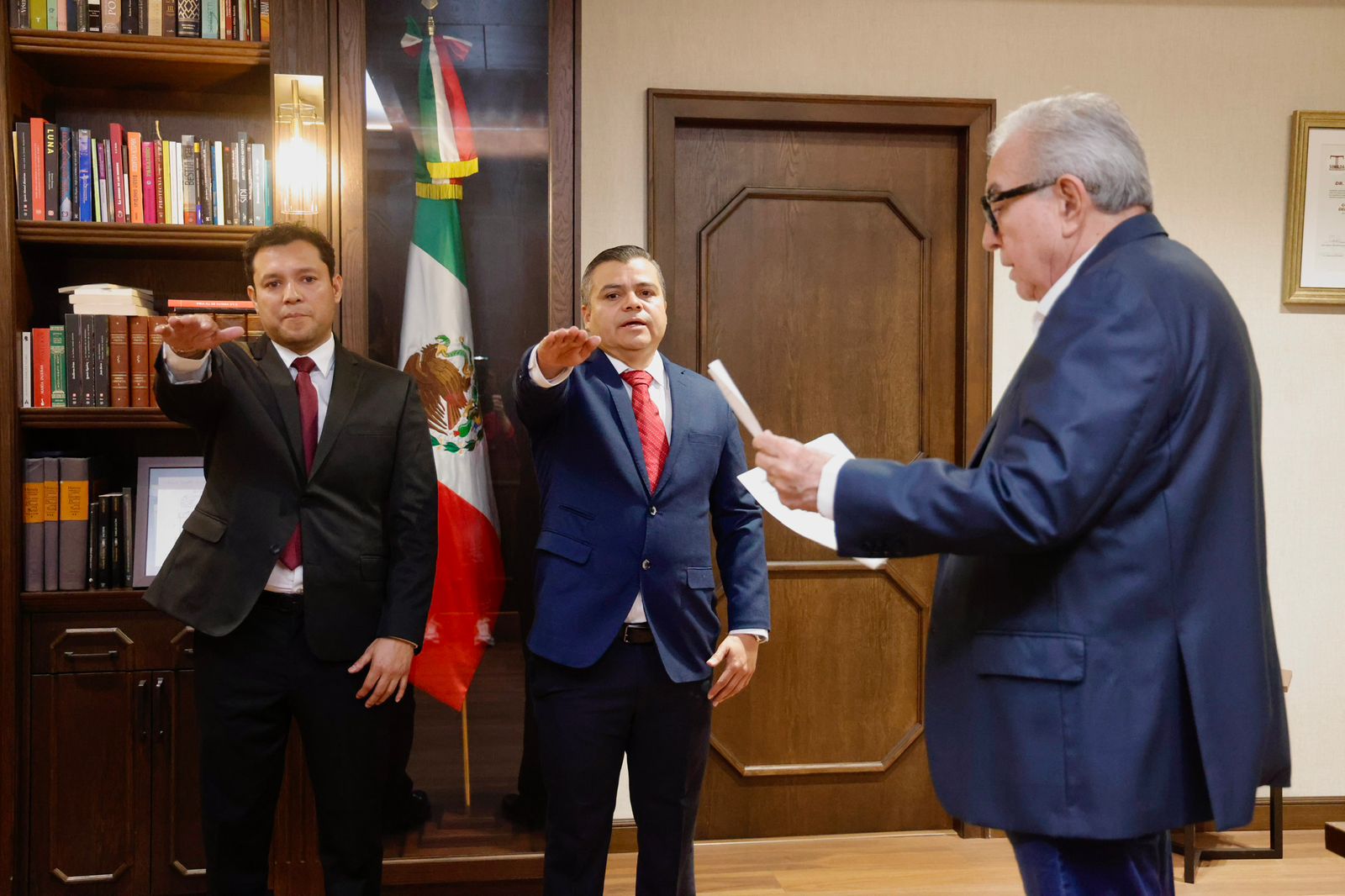 Dos funcionarios con el brazo levantado a manera de juramento y Rocha leyendo un documento