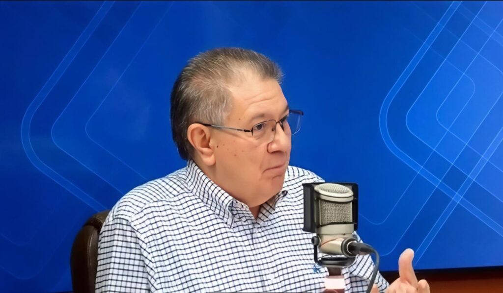 Una persona en un estudio de grabación con un fondo azull y frente a él, un micrófono