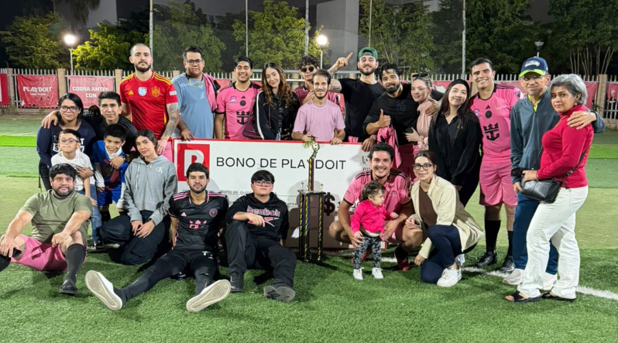 Personas sosteniendo un cheque enorme y un trofeo, dentro de una cancha de futbol, posando para la foto