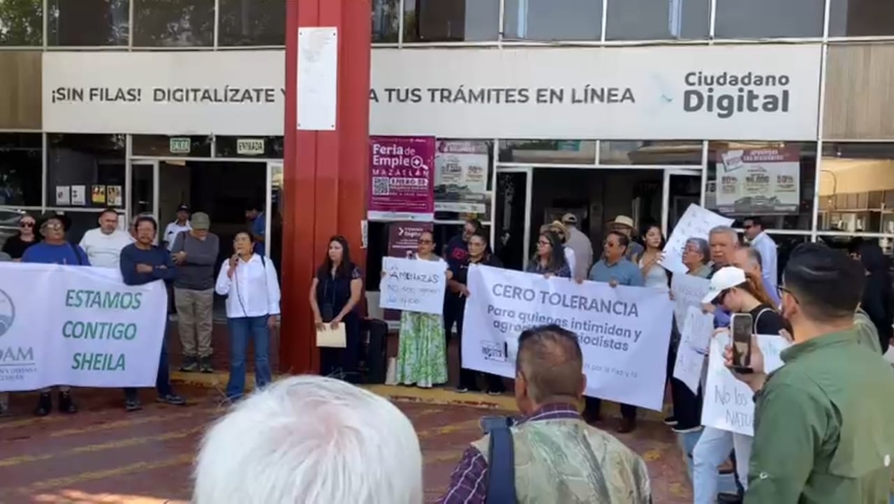 Personas realizando una manifestación sosteniendo carteles y hablando por micrófono