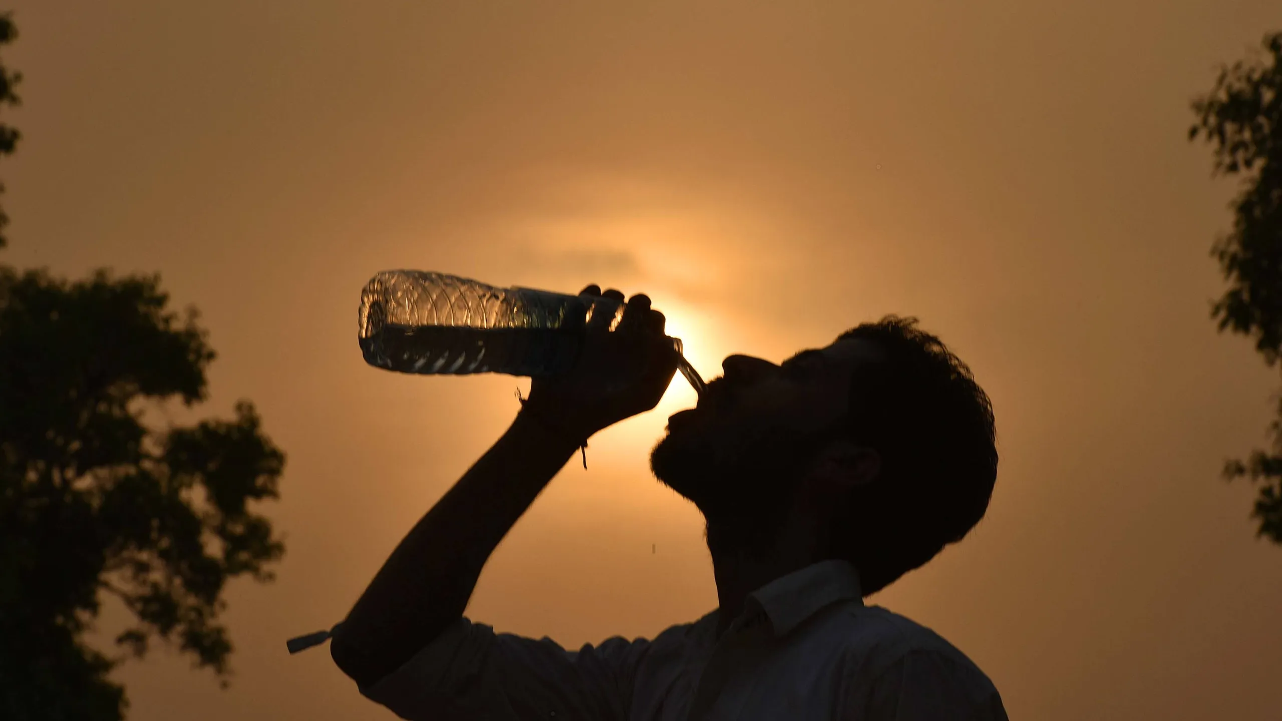 sombra de una persona tomando agua de una botella y al fondo el sol ardiente