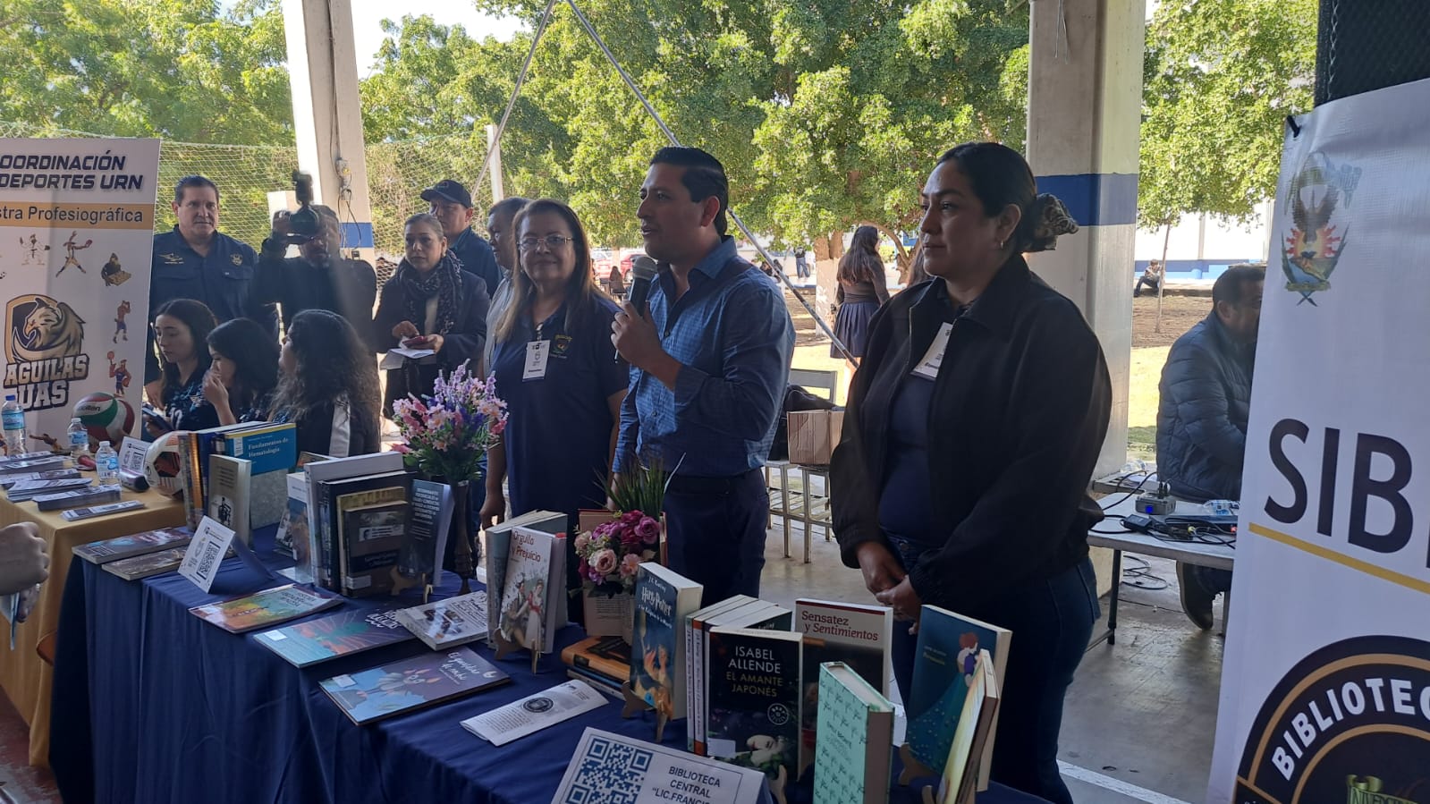 Personal de la UAS detrás de una mesa con libros en exhibición