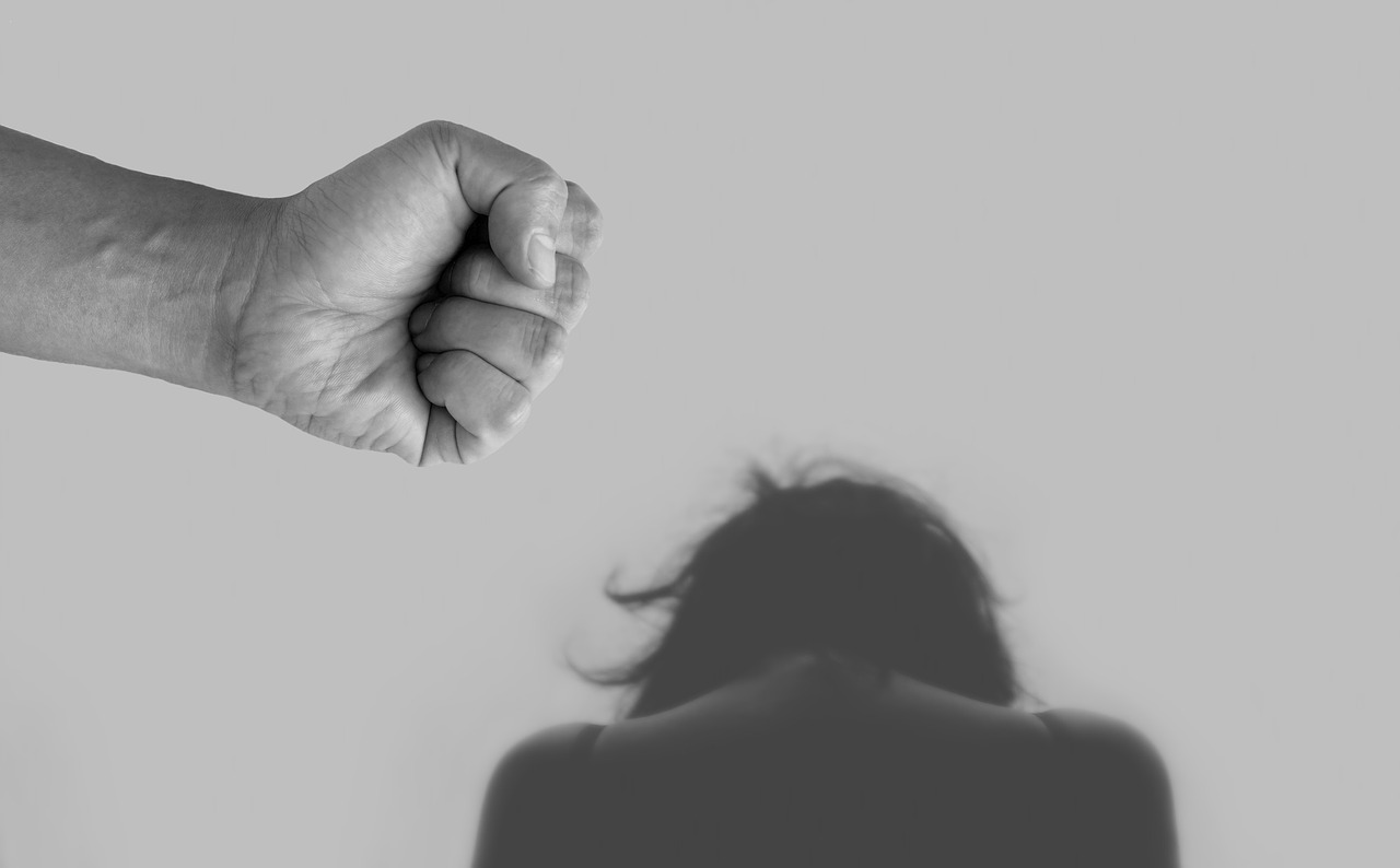 Puño de un hombre y detrás la silueta de una mujer agachada