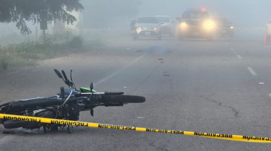 Cinta amarilla de precaución en una calle en la que hay una motocicleta tirada y carros al fondo