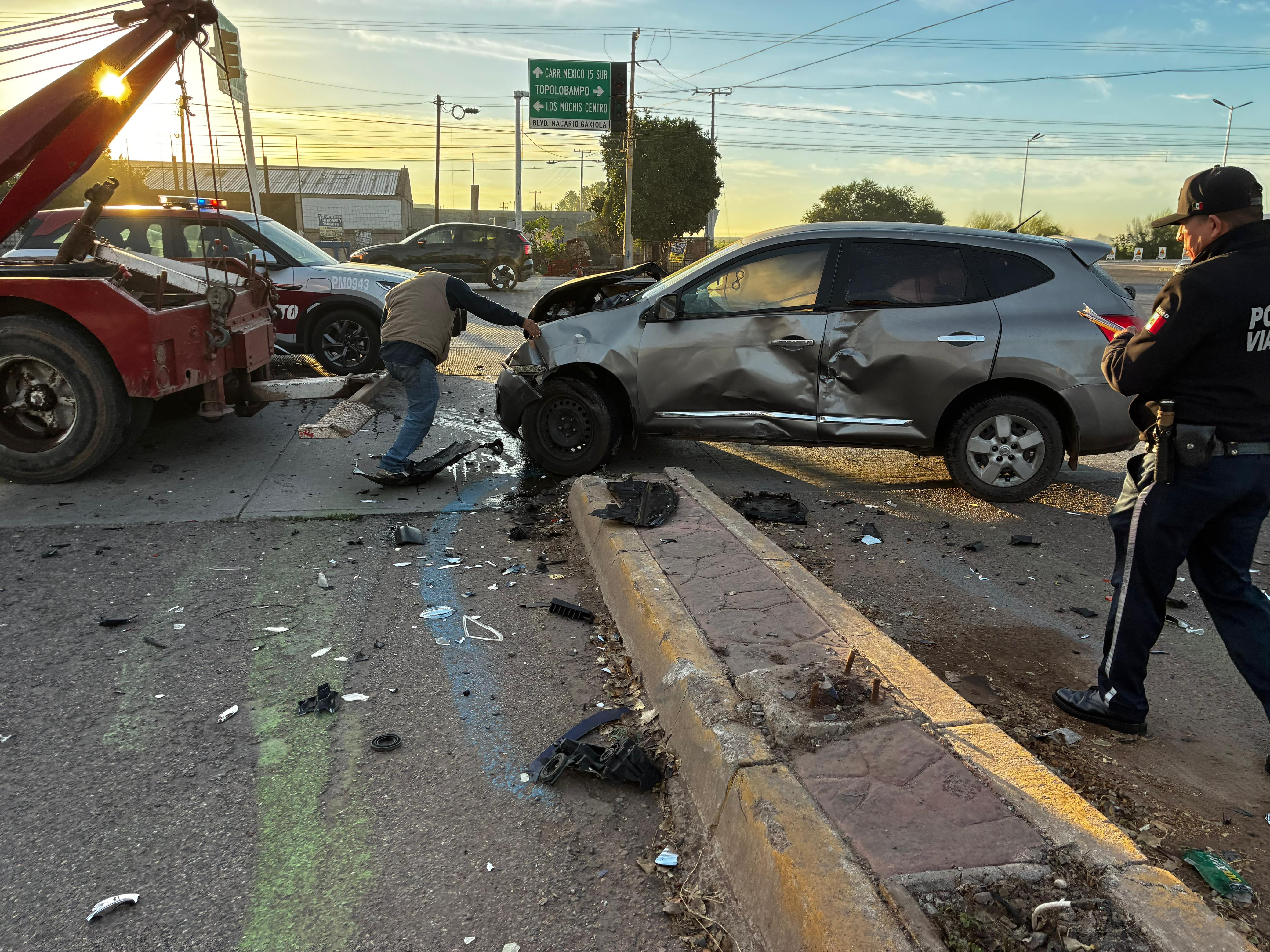 carro color gris con golpes en una calle junto a una grúa roja y un elemento policiaco