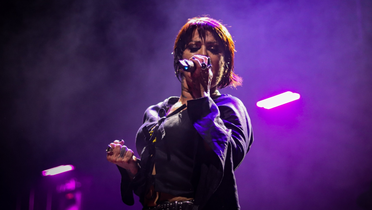 Alejandra Guzmán cantando en un concierto con un fondo morado