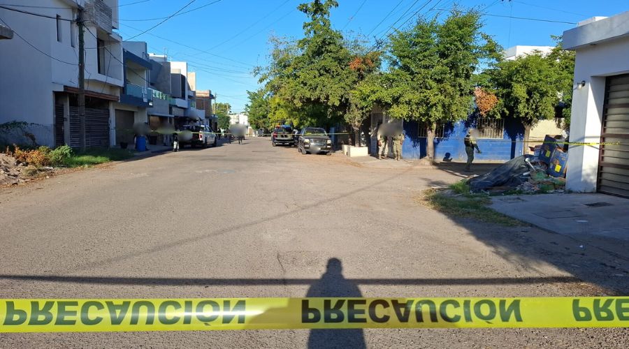 Cinta amarilla de precaución y un elemento policiaco, al fondo se osbervan varias unidades del Ejército Mexicano y elementos desplegados en una calle