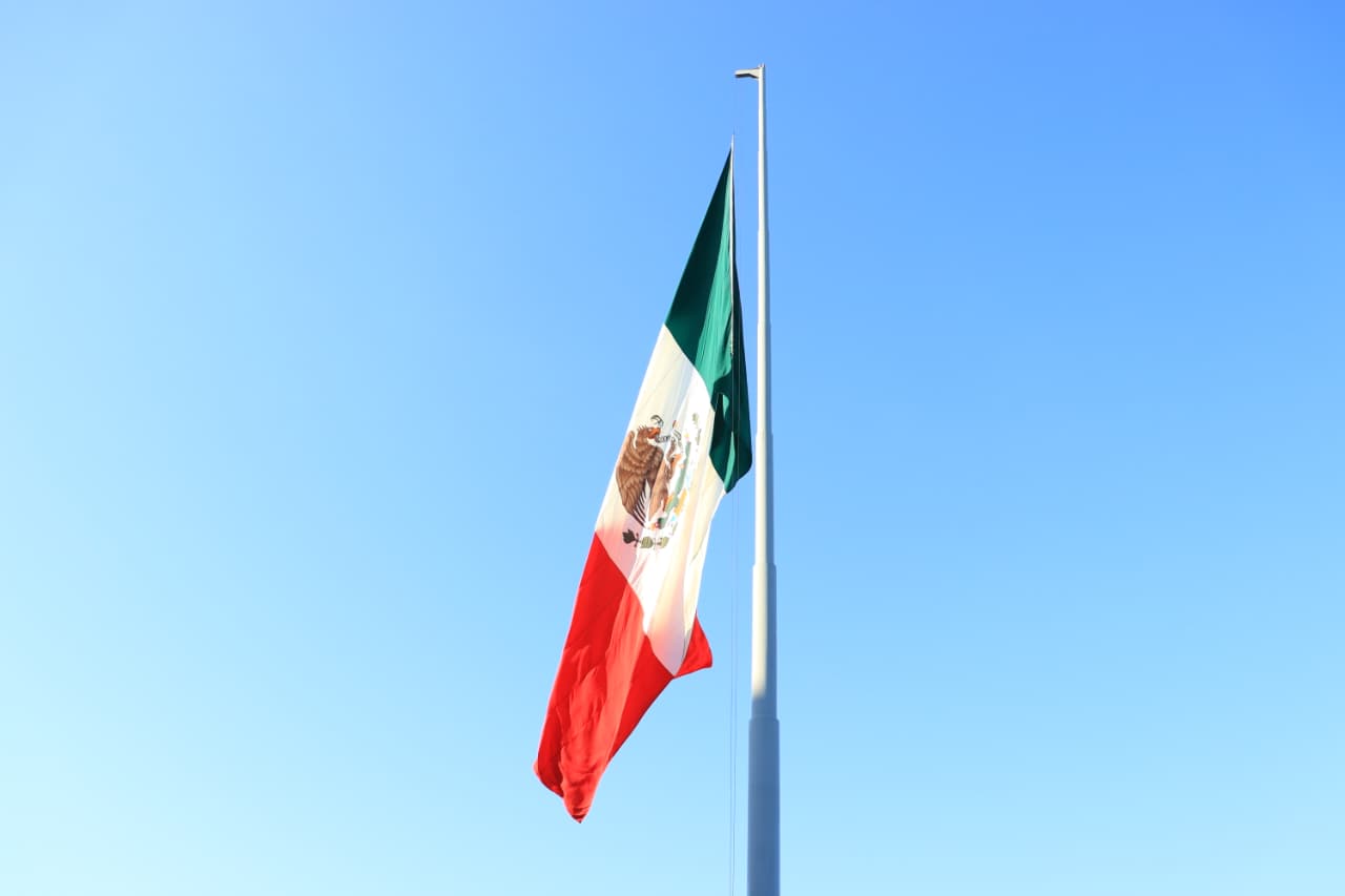 bandera de méxico en asta con cielo azul soleado de fondo