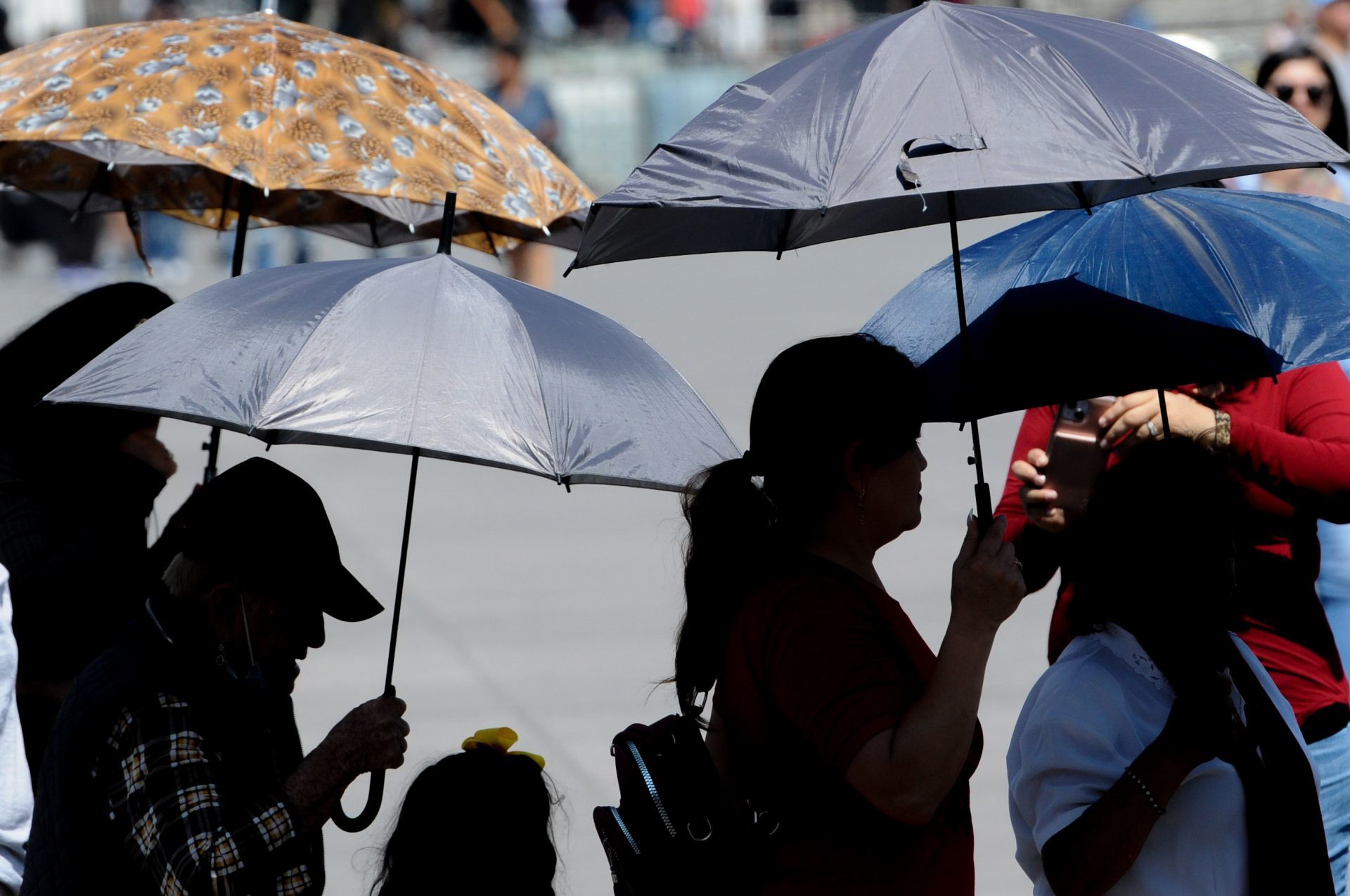 personas con sombras y en silueta caminan con paraguas para cubrise el sol
