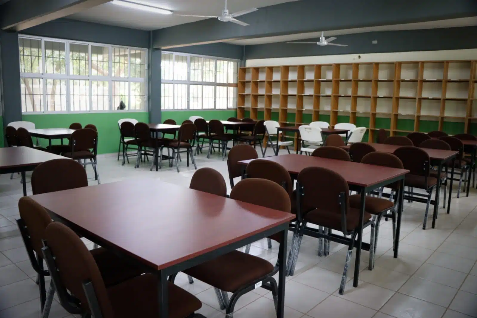 Salón de clases con mesas, sillas y librero al fondo