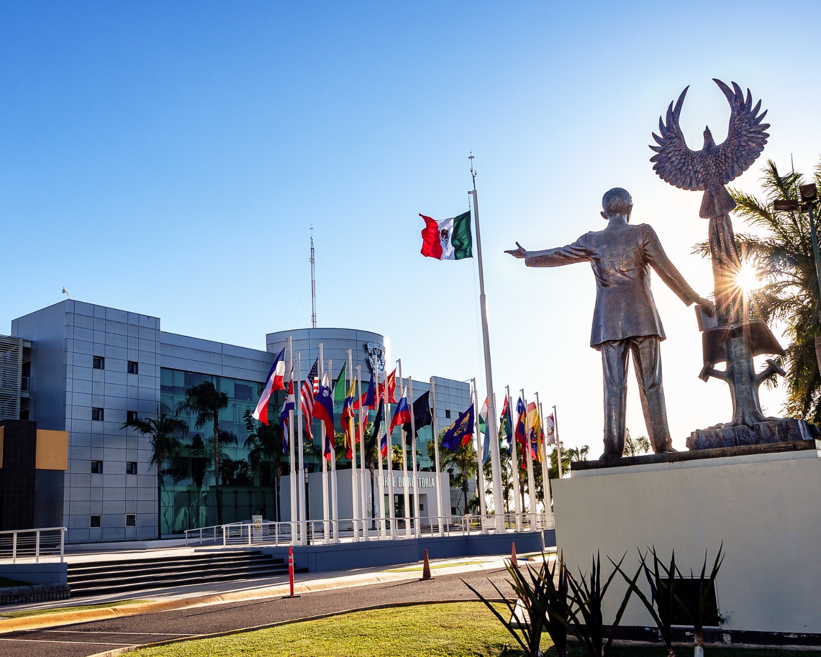 edificio de la uas con banderas de diferentes paises y monumento representativo con cielo soleado de fondo