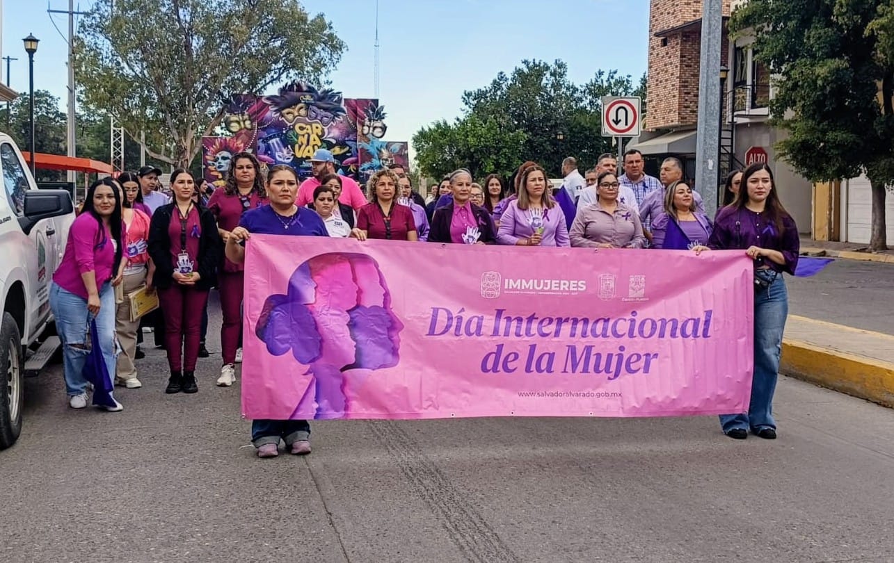 Personas sosteniendo una lona rosa y atrás de ellas un grupo de personas