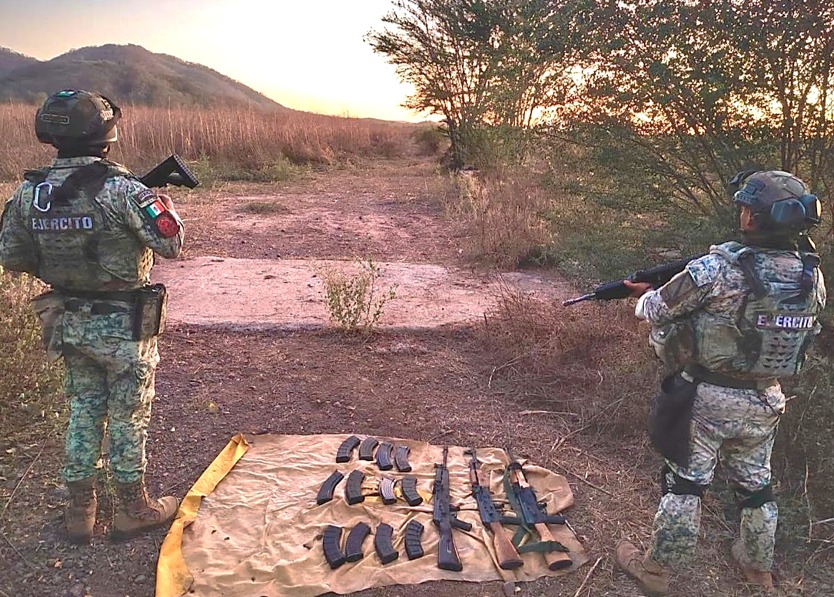 Elementos del Ejécito Mexicano parados y en el suelo una sabana verde y sobre ella artefactos y armas