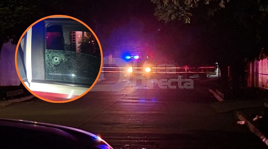 Patrulla con luces encendidas en una calle y en un círculo un vidrio de una unidad policiaca con un impacto de bala