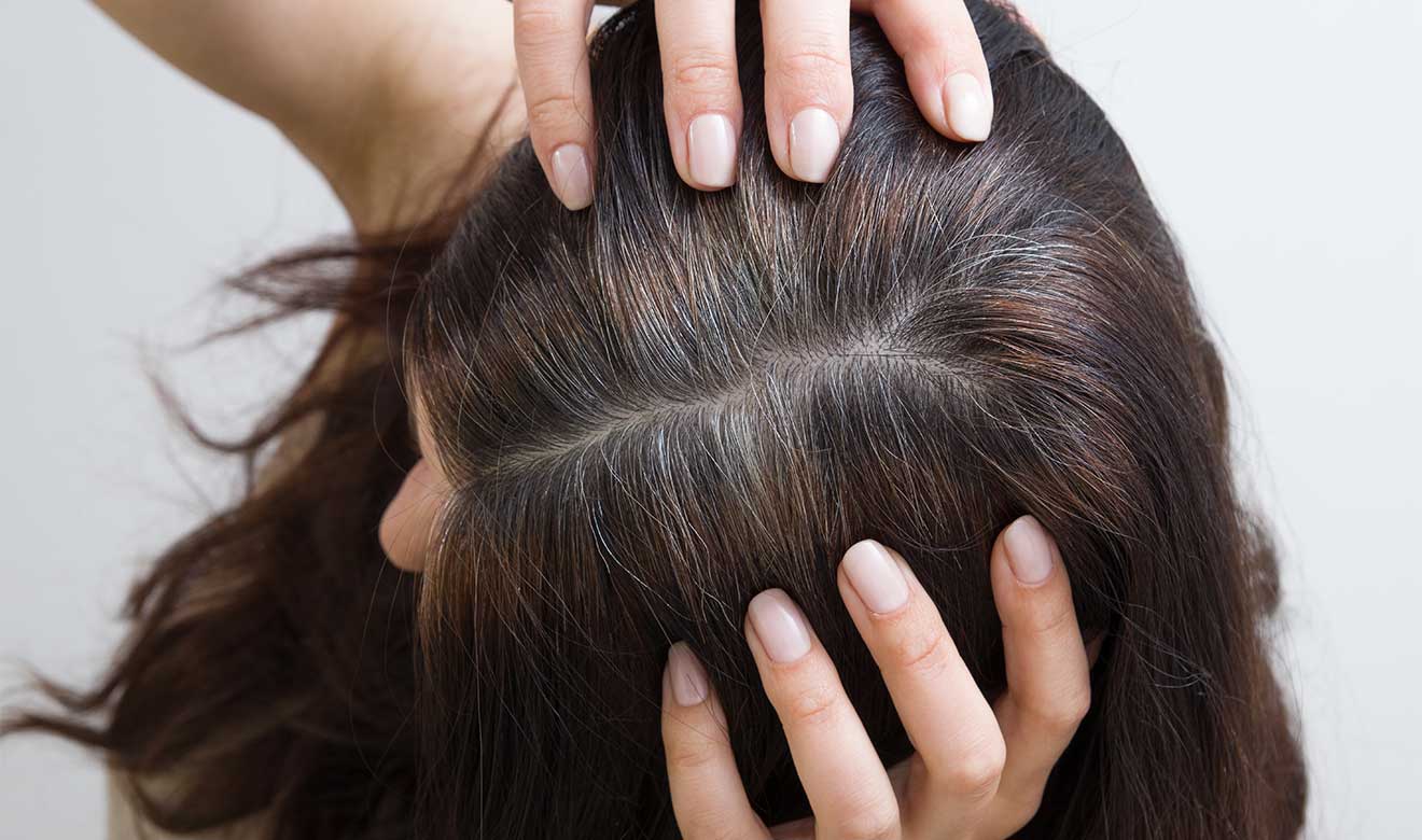 mujer con las manos en su cabeza y despejando su cabello de color café oscuro con canas