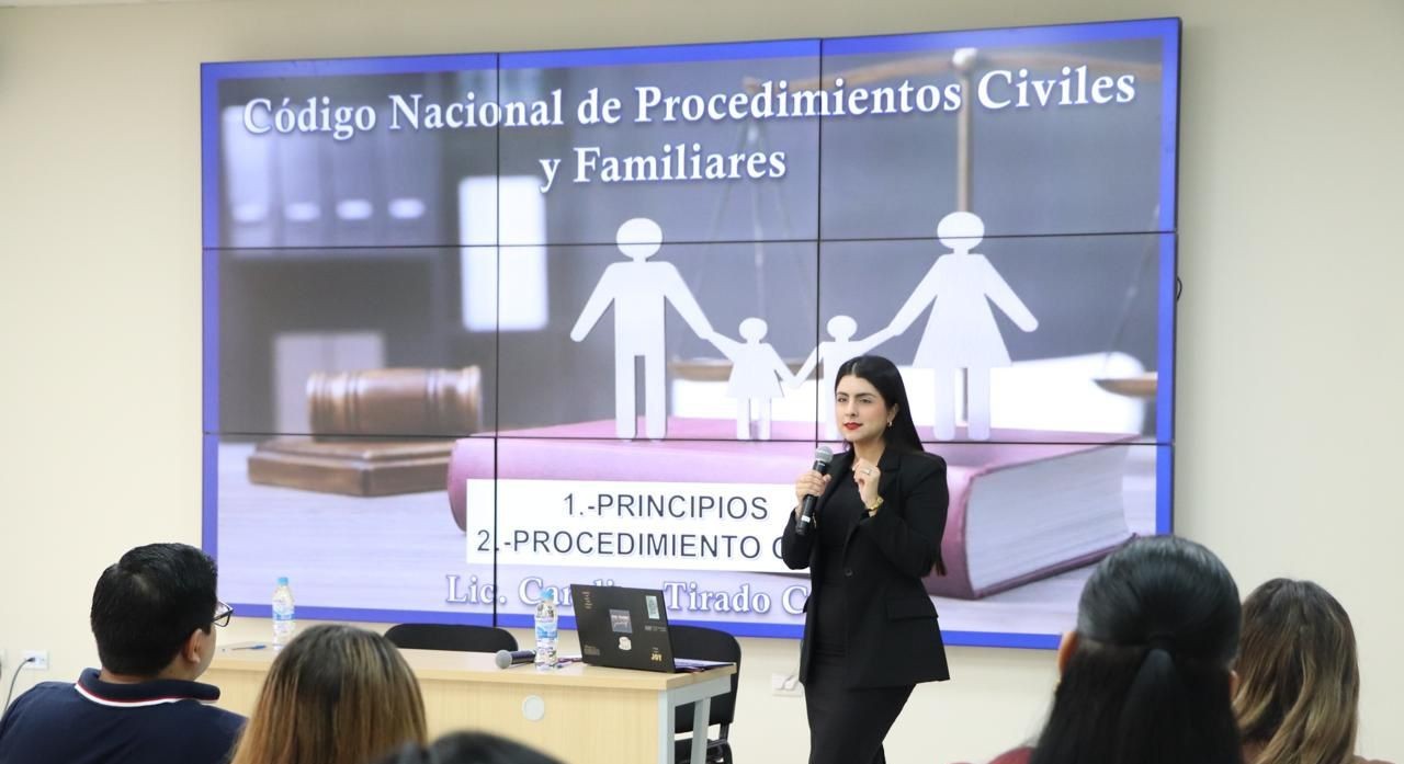 Funcionaria hablando frente a personas, con proyector encendido