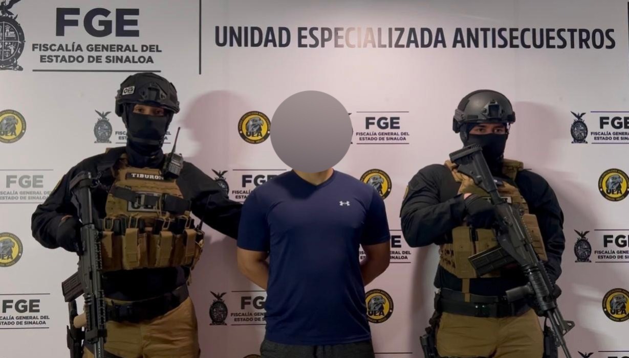 Elementos de seguridad a los lados de un detenido con la cara blureada