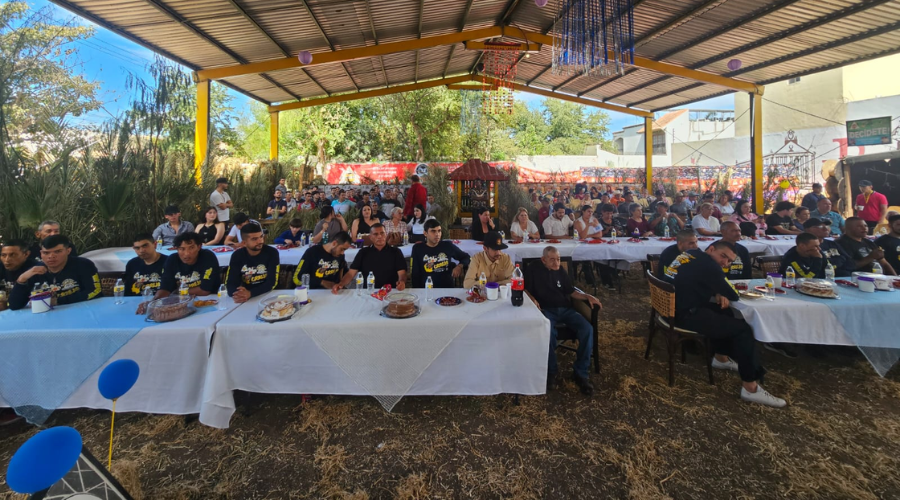 Grupo de personas bajo una techumbre, sentados en mesas