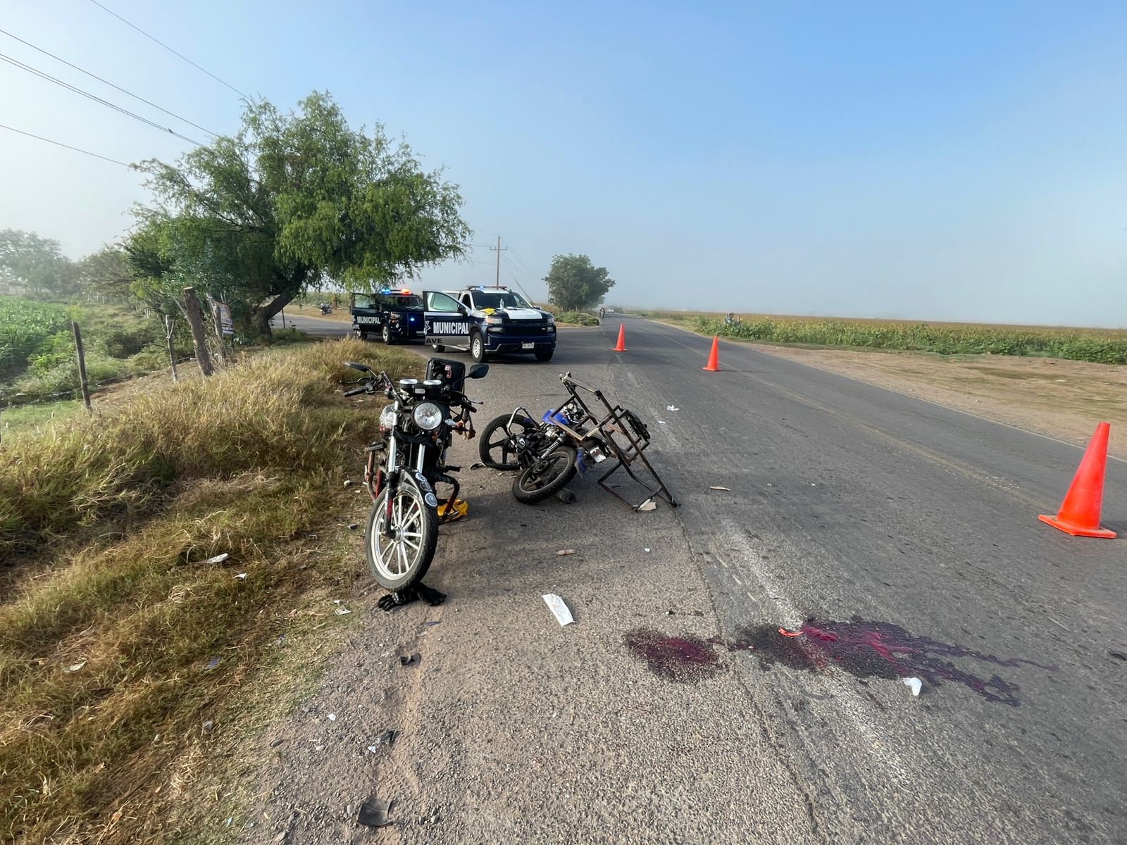 Dos motos estacionadas en orilla de carretera y al fondo unidades de policía