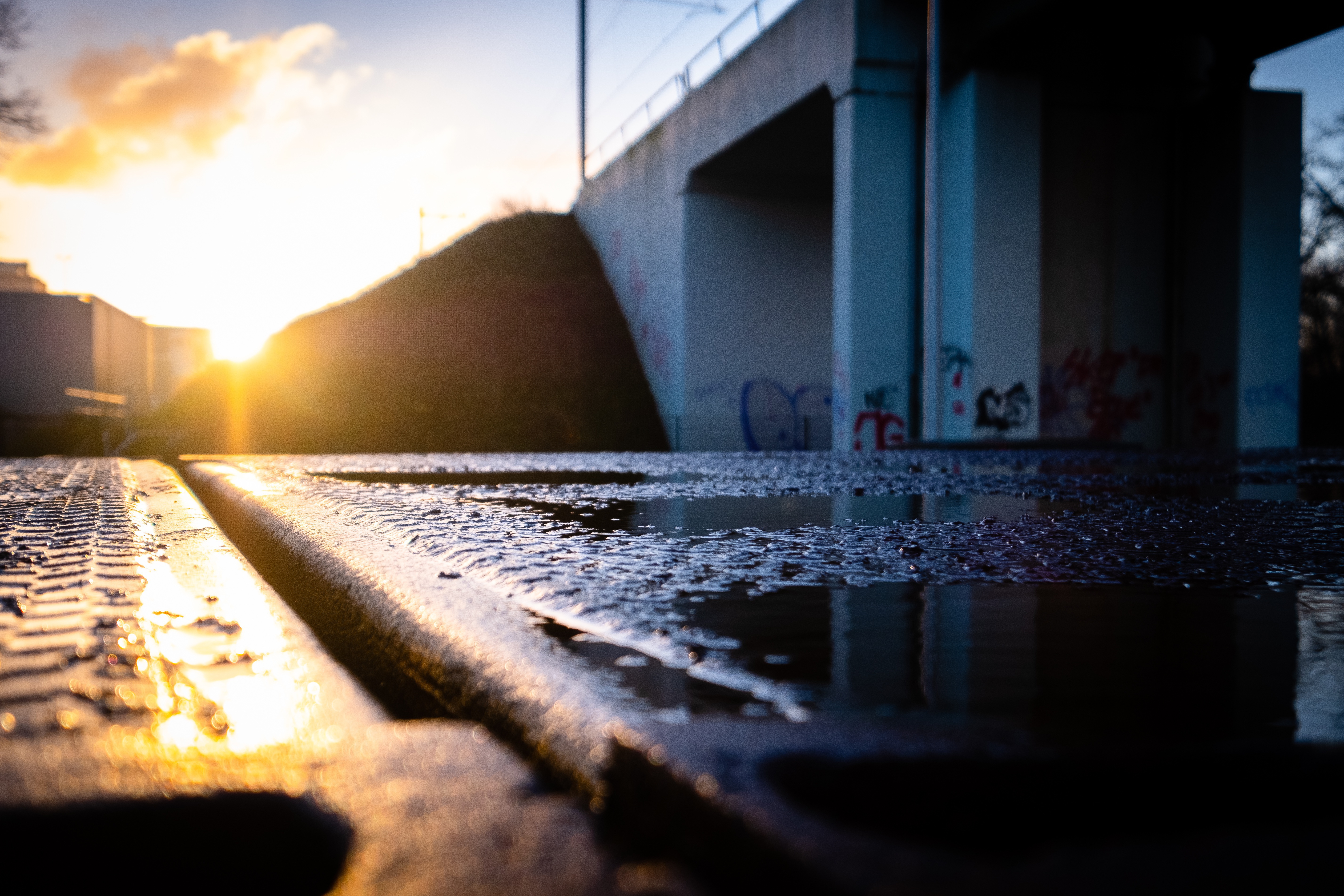 Calle bajo mojada luego de la lluvia y al fondo se observa un puente y el sol en el cielo con algunas nubes