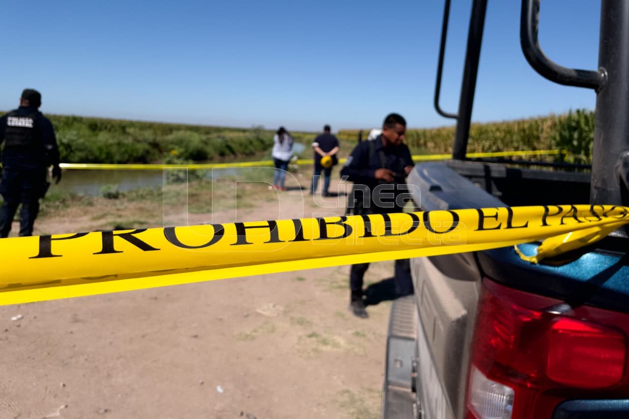Cinta amarilla precaución junto a una patrulla y elementos policiacos en una zona de sembradios