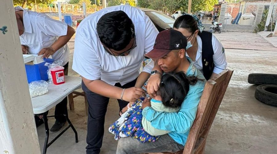 Enfermero aplicando vacuna a una infante que está siendo sostenida por un adulto mayor