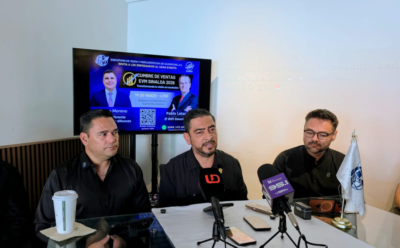personas en una rueda de prensa con micrófonos al frente y una pantalla en el fondo