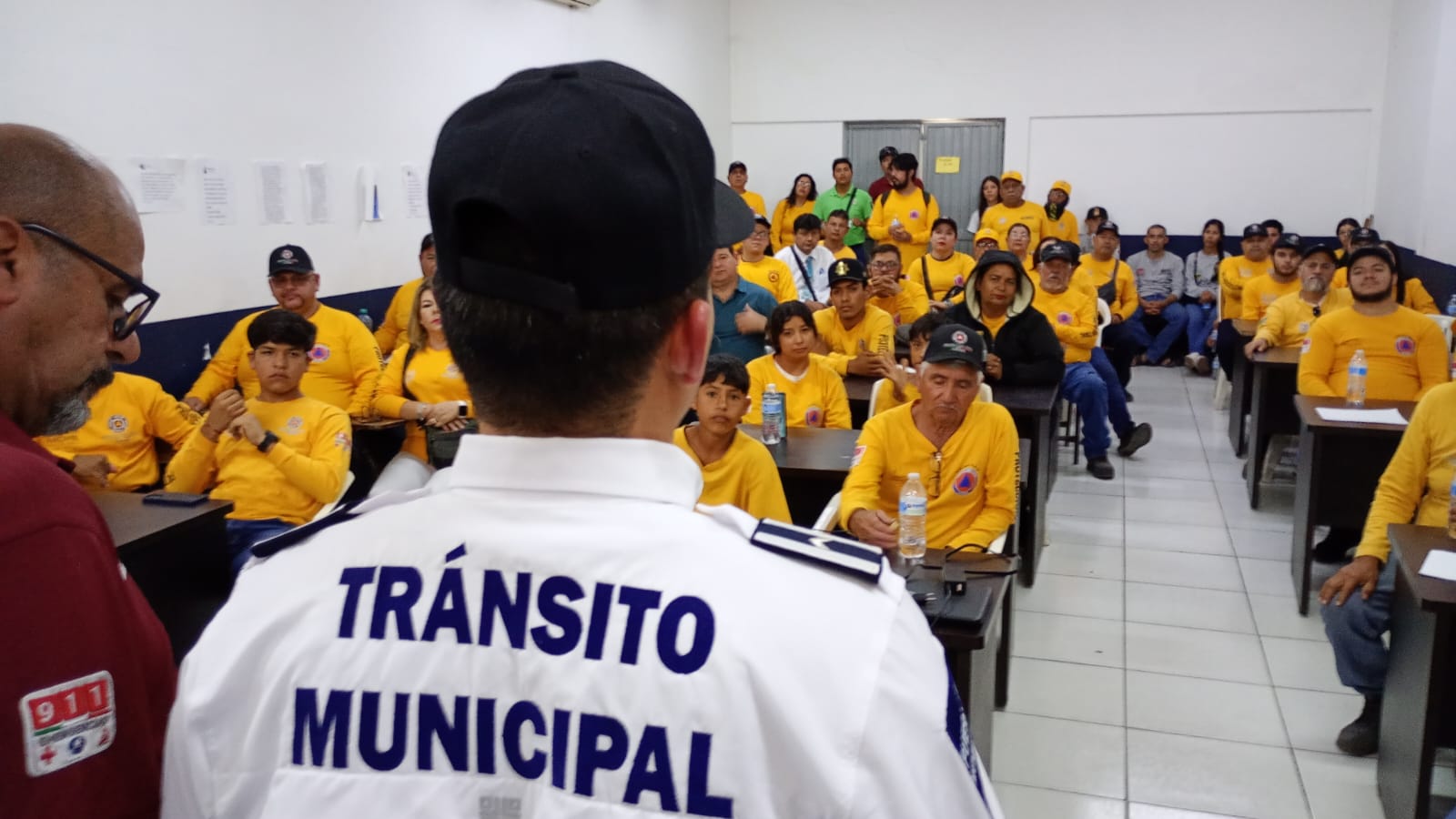 Espalda de Tránsito Municipal frente a personas sentadas de color amarillo