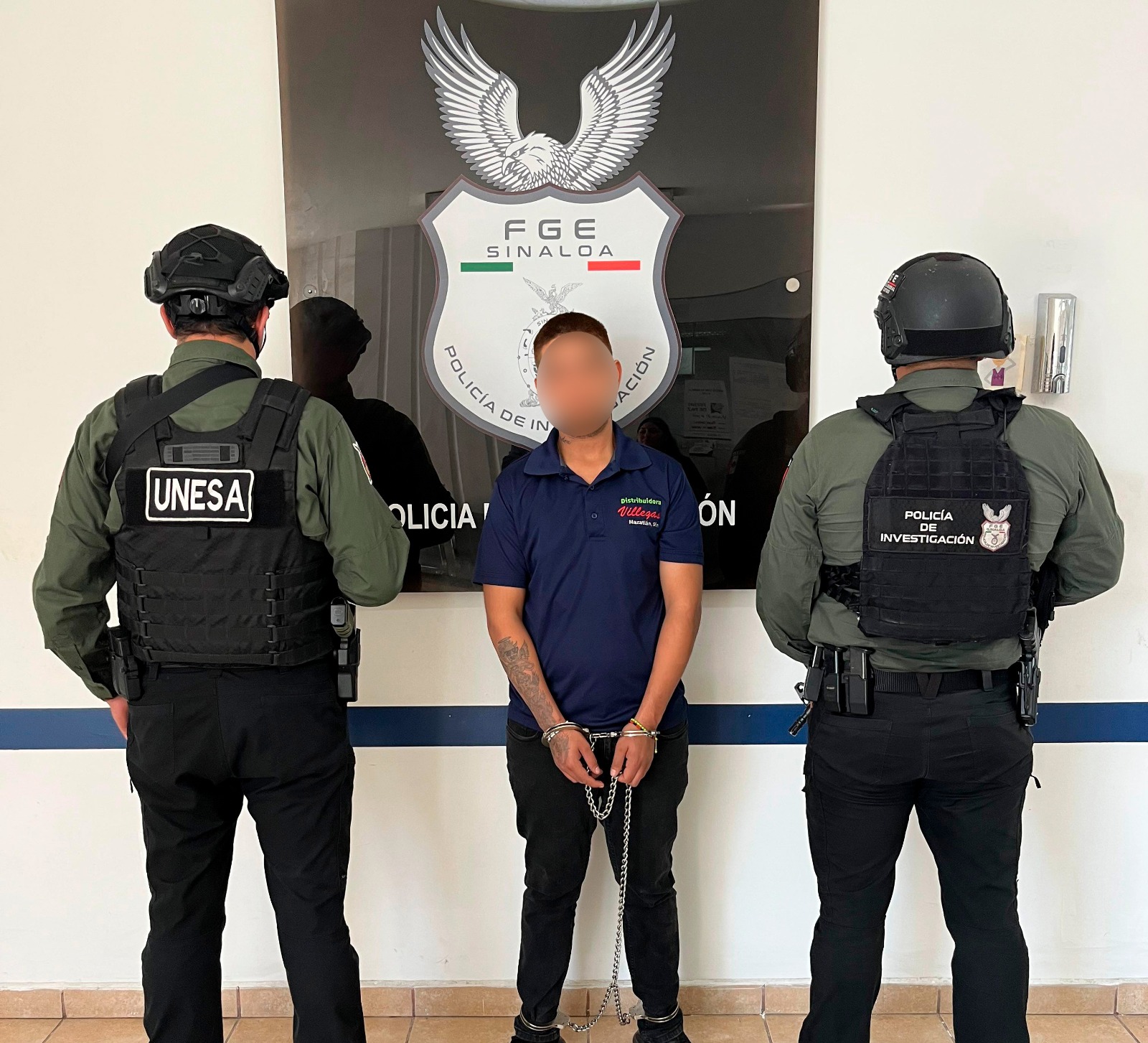 Dos elementos de seguridad junto a una persona detenida con difuminado en la cara
