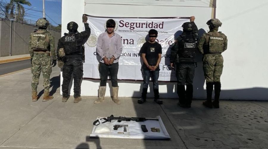 Dos jovenes detenidos con cintillo en los ojos tapándoles el rostro, elementos de seguridad al lado de ellos y artefactos confiscados en el suelo
