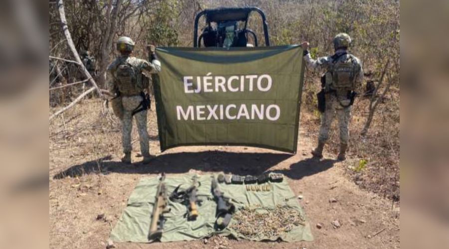 Elementos del ejercito de espaldas sosteniendo una pancarta y debajo de ellos artefactos confiscados