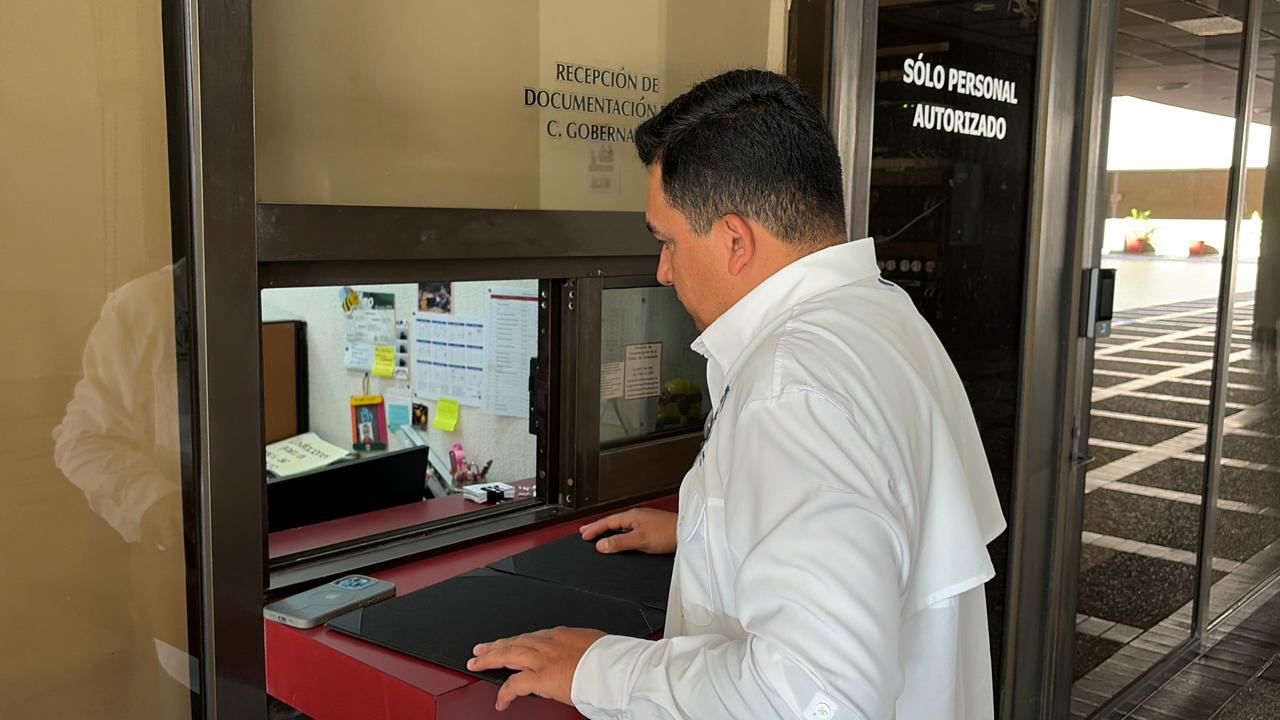 Funcionario entregando documentos por ventanilla a departamento de Gobierno