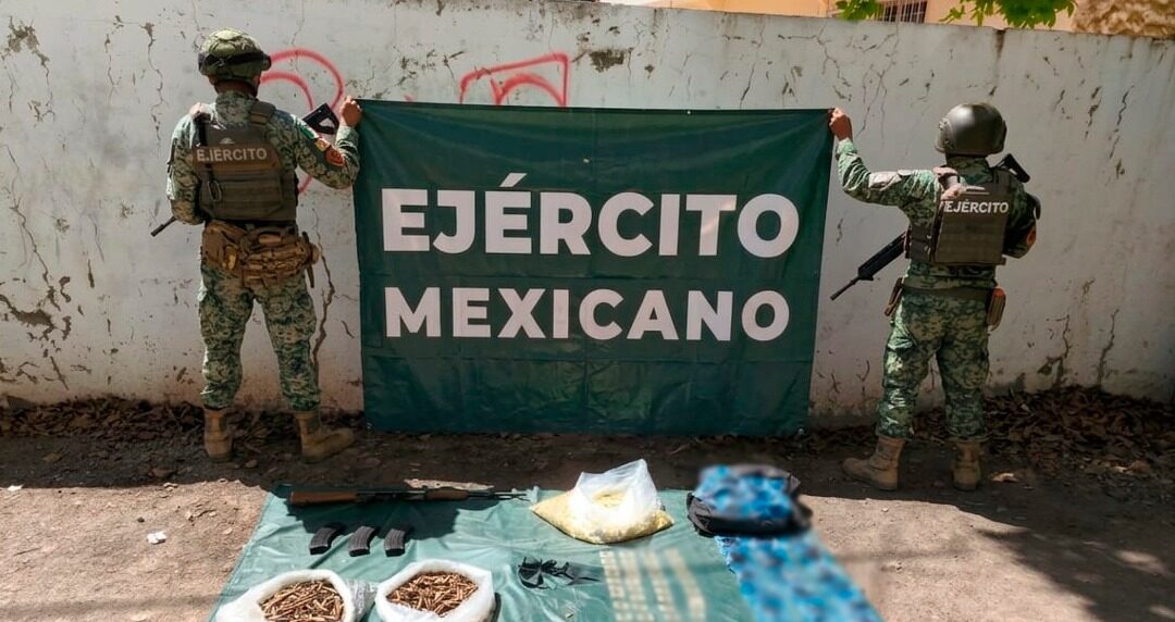 Dos elementos del ejército mexicano con una lona junto a aseguramiento de armas tiradas en una manta