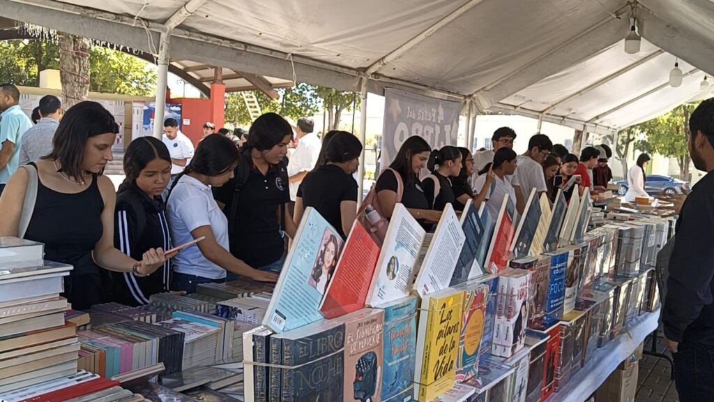 Libros apilados en una mesa junto a muchas personas en eventos