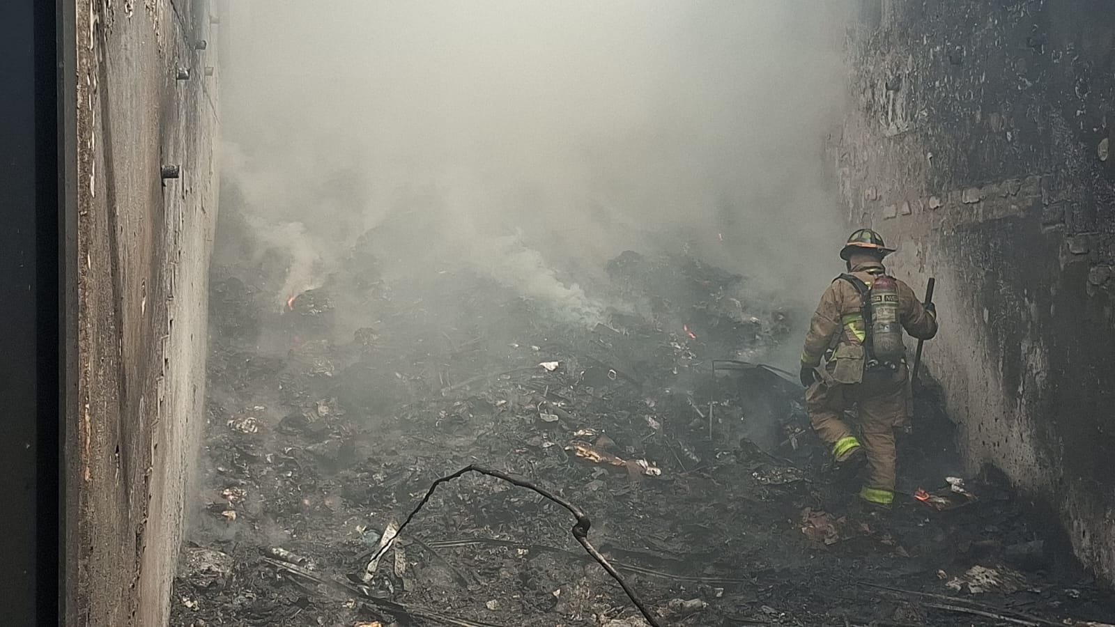 Lugar con daños por incendio y el humo esparciéndose mientras un elemento de bomberos revisa la zona