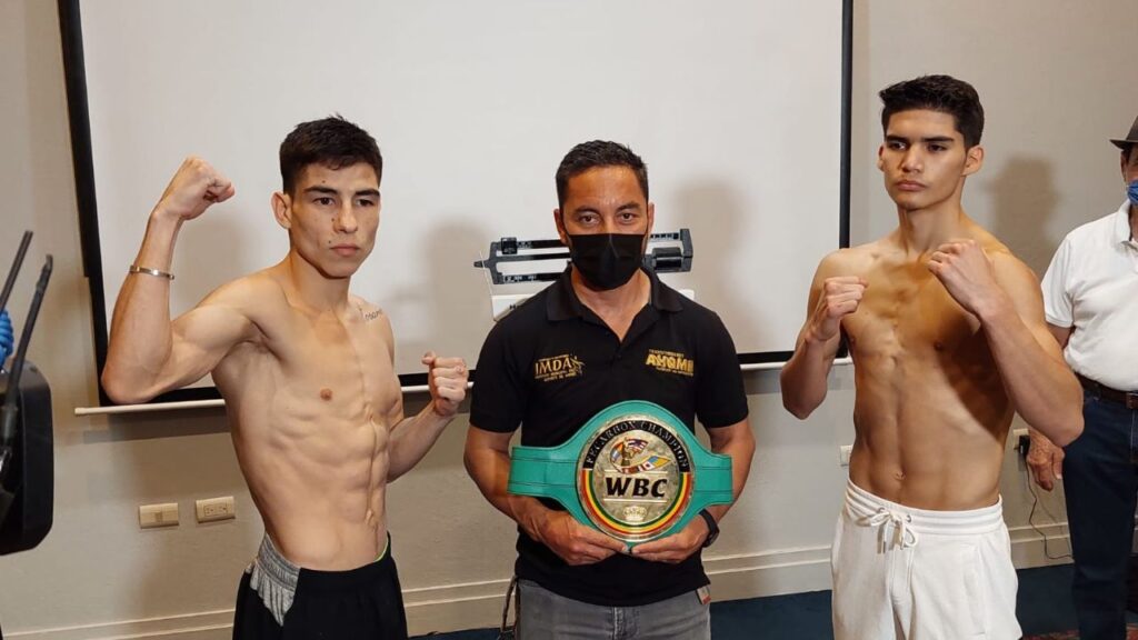 Peleadores de box posando, una persona en el medio sosteniendo un campeonato
