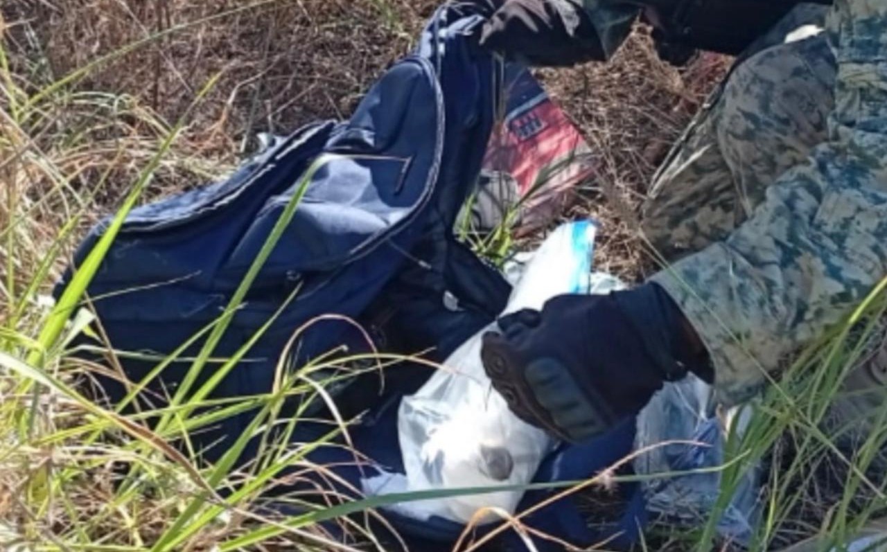 Manos de una persona (militar) junto a una maleta negra con objetos y billetes falsos