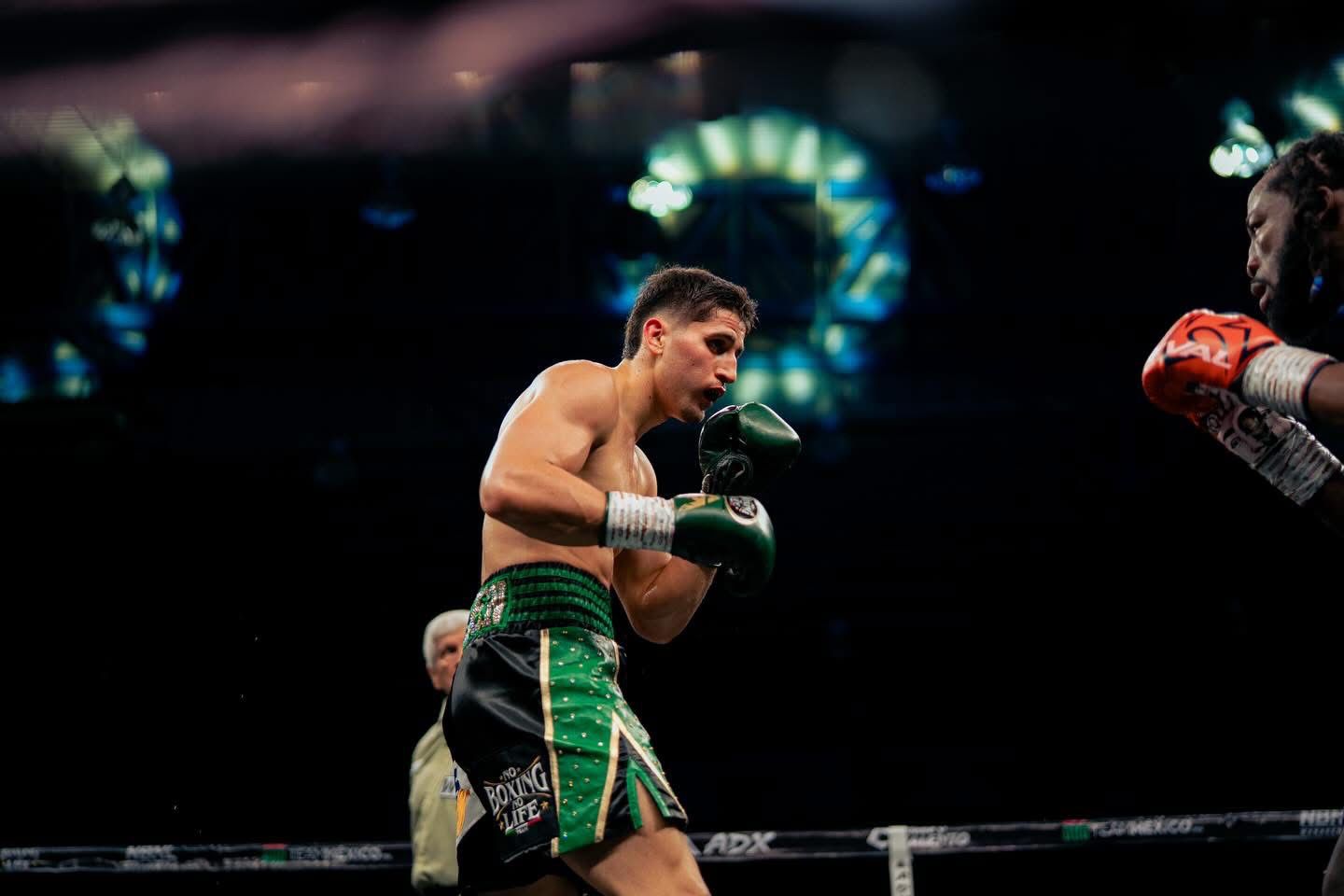 marco verde boxeando con short verde y guantes de box negros. luces detrás de él