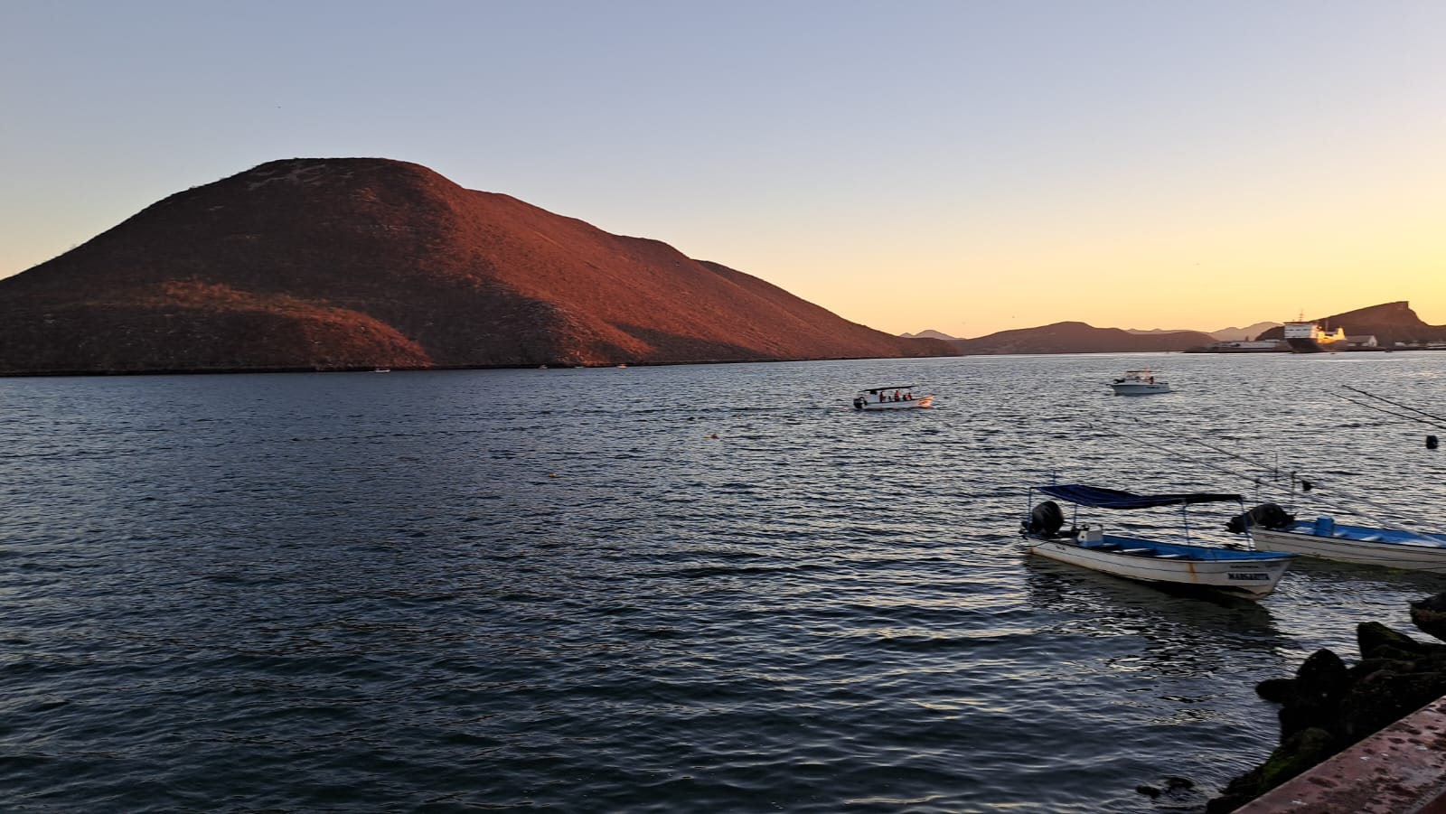 Mar donde se ven lanchas estacionadas en el puerto y un pequeño cerro al fondo